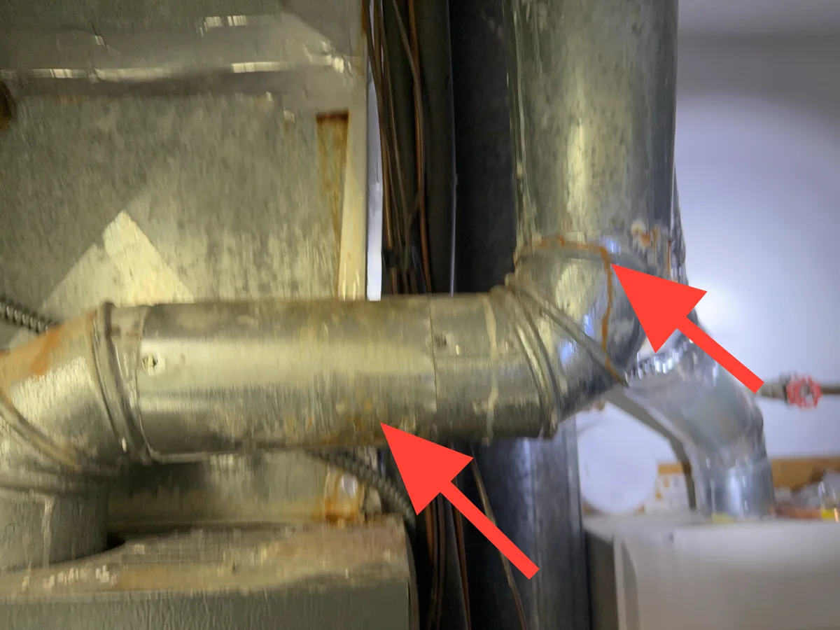 Rust streaks on a furnace vent connector above the cabinet
