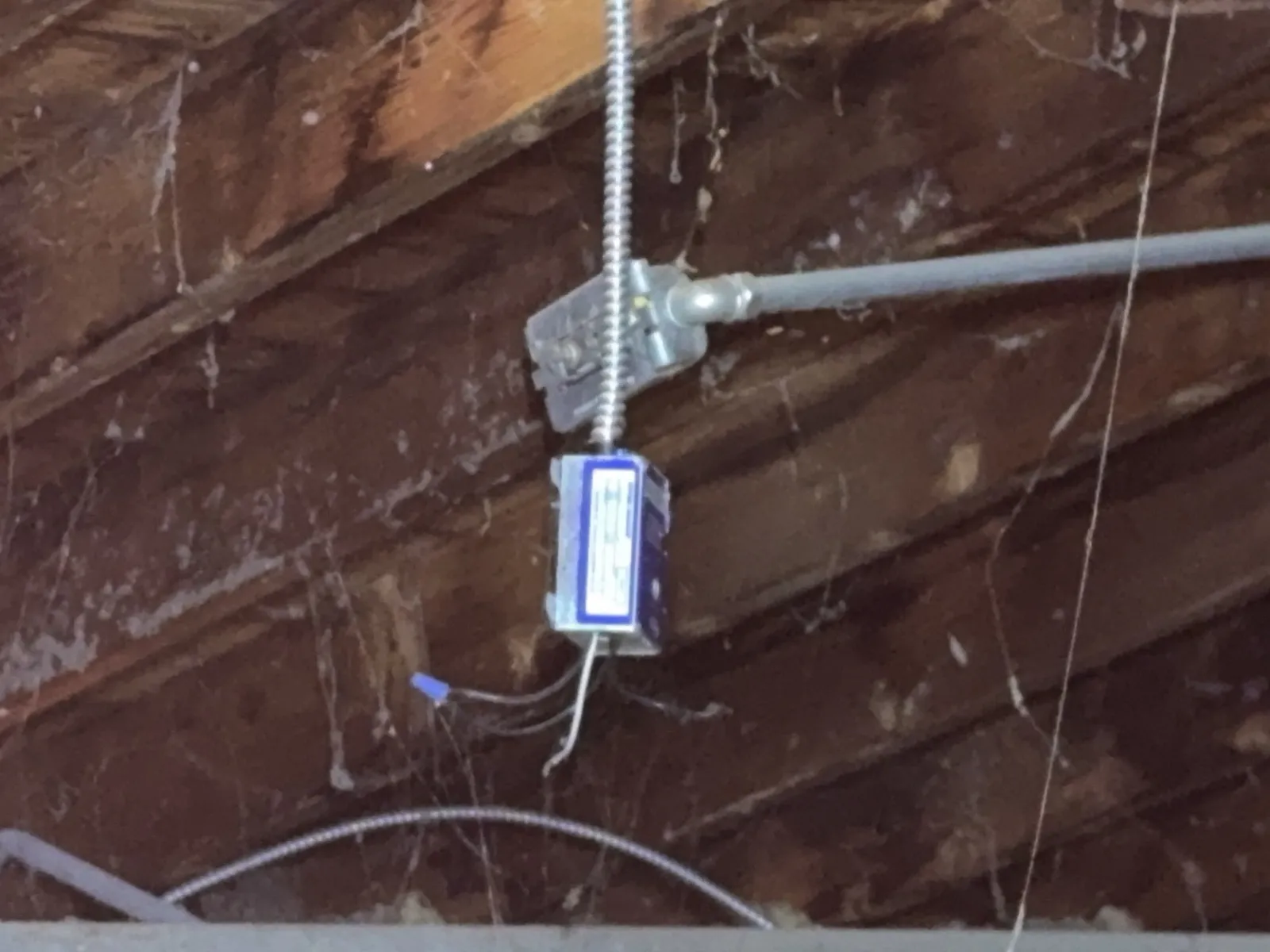 Electrical conductors hanging loose below a junction box mounted on an attic rafter