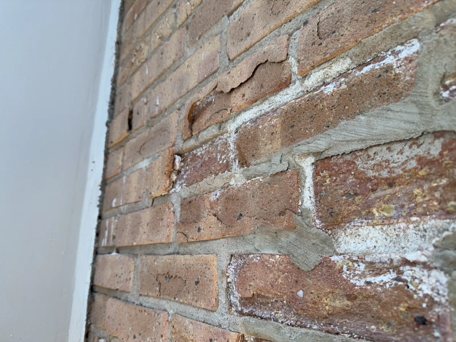 Close view of brick with flaked-off faces and white deposits along the mortar joints