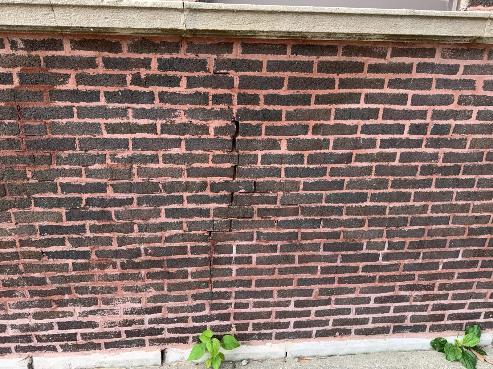 Vertical crack running through the bricks themselves below a stone window sill on a red brick wall