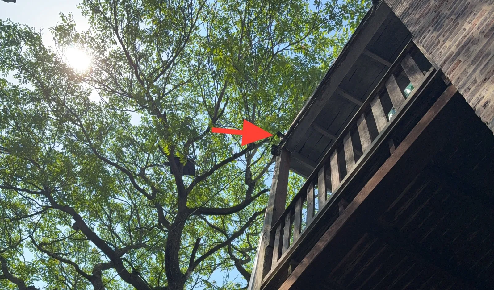 Looking up at a wood rear porch on a brick building, with an arrow pointing to the service drop attachment beside the landing