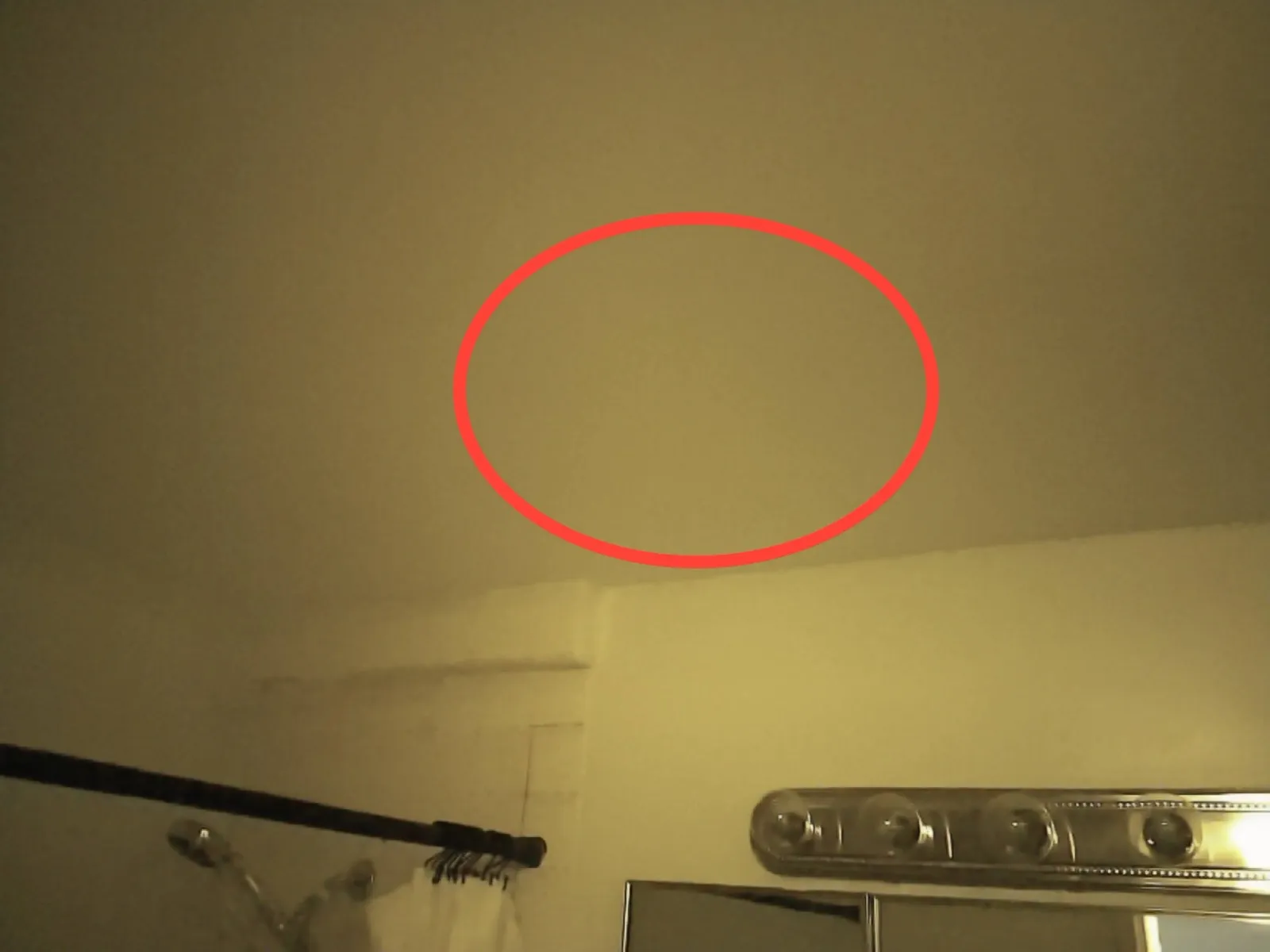 Bathroom ceiling with a red circle marking the area above the toilet, no visible staining