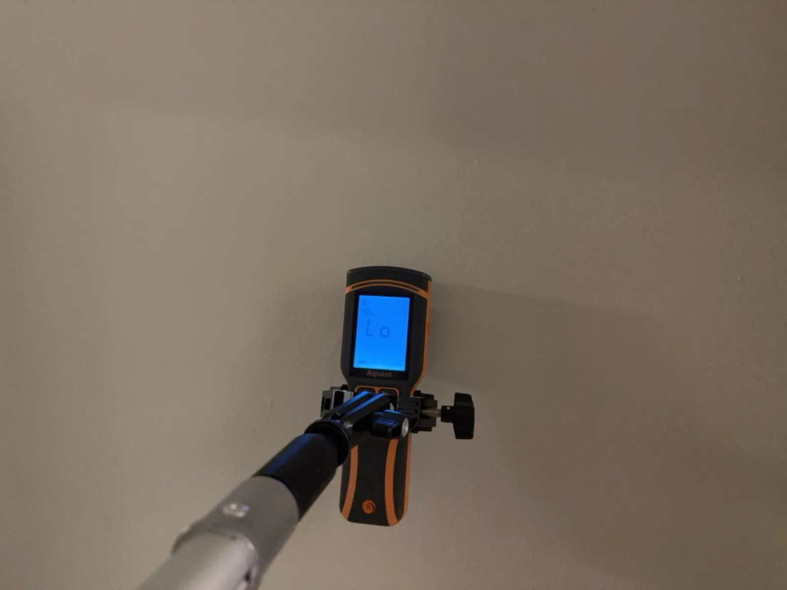 Moisture meter on a pole against a ceiling, its screen reading Lo