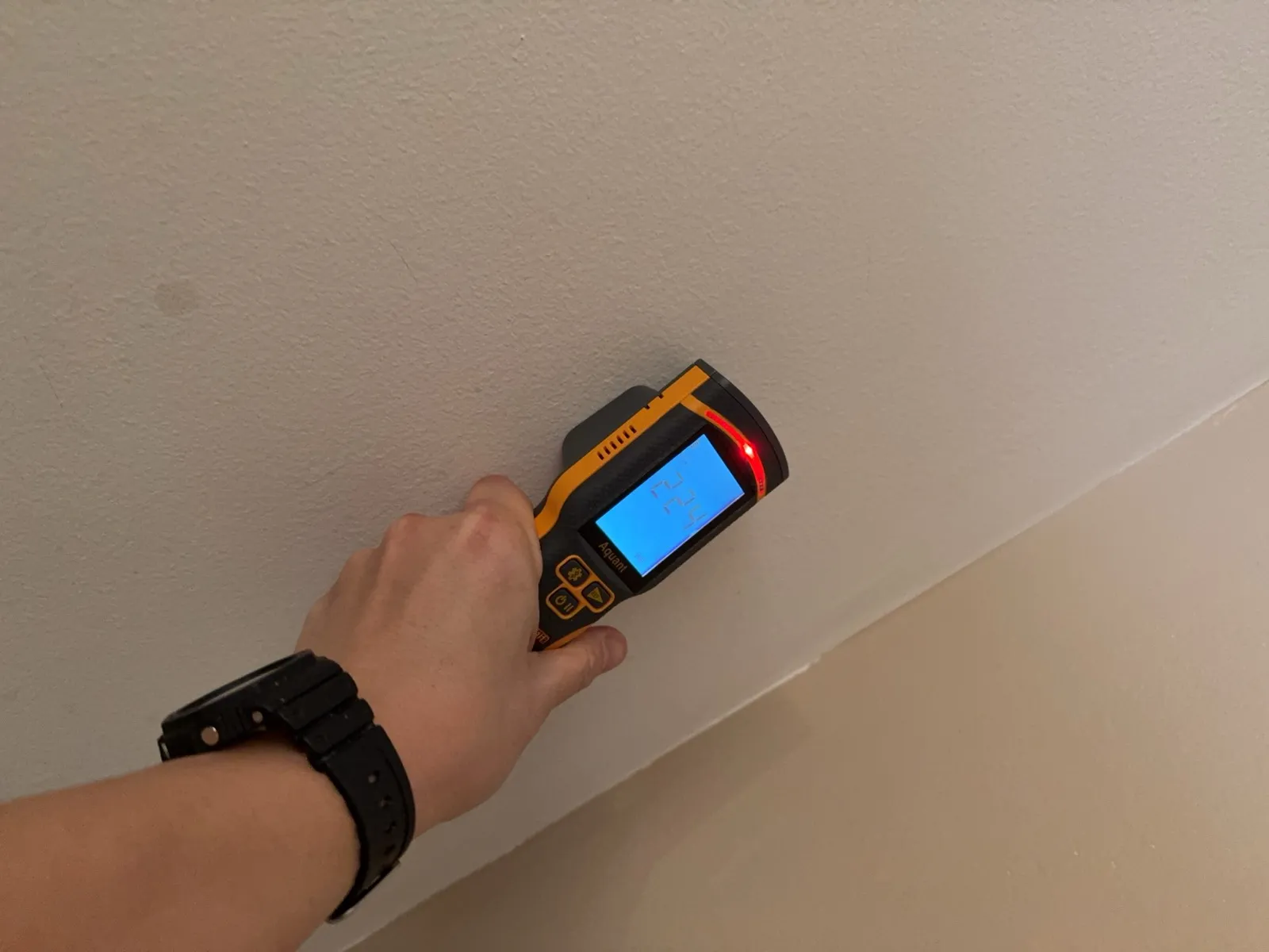 Pinless moisture meter held against a bathroom ceiling, its red wet indicator lit