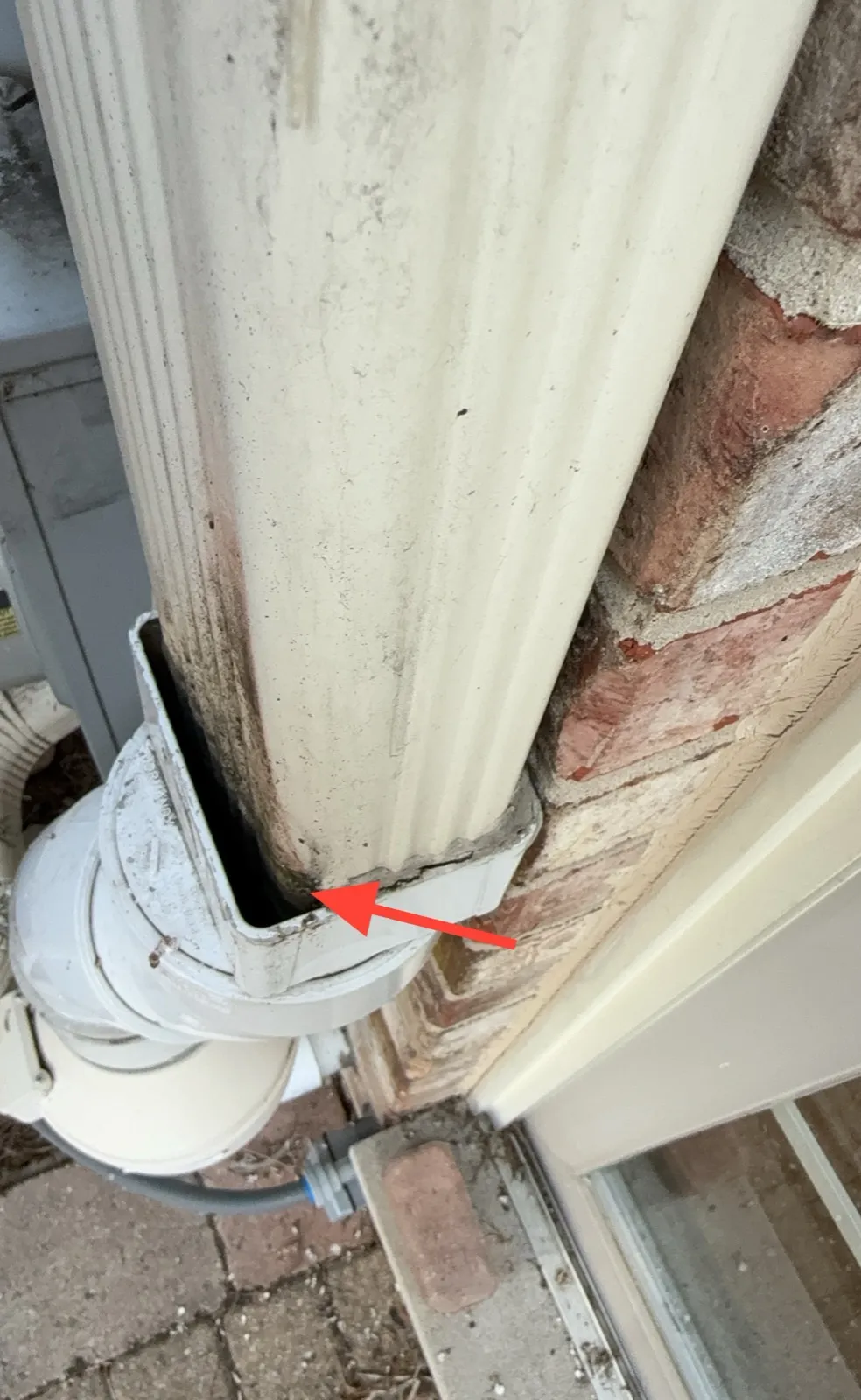 Rectangular downspout section of an exterior radon vent with an open gap at its joint with the fitting below, marked with a red arrow